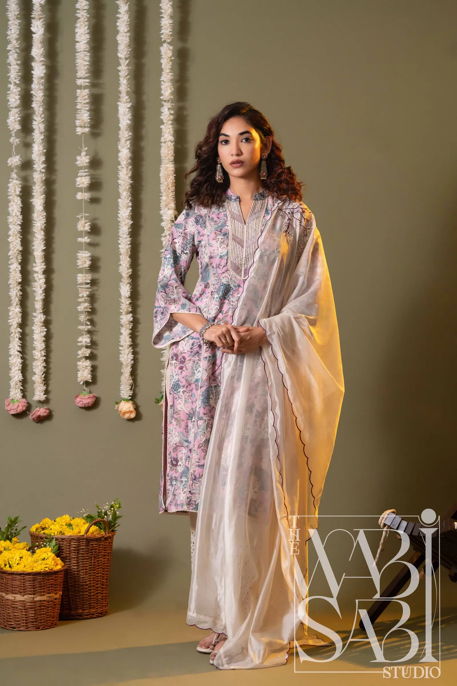 Model in a lilac printed kurta and ivory dupatta beside flower garlands