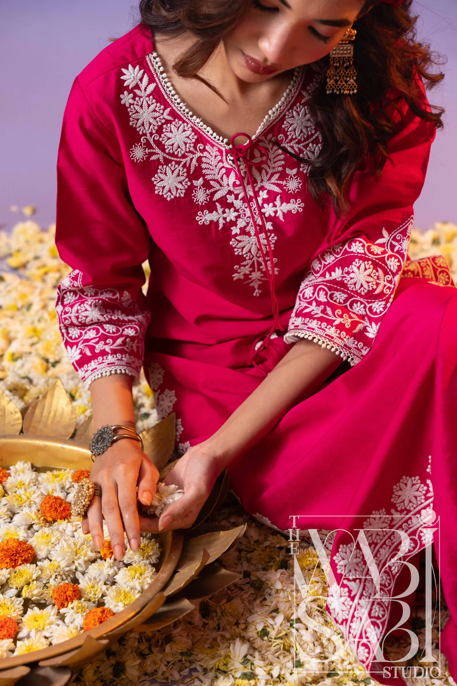 Model in a pink embroidered kurta sorting flowers in a brass bowl