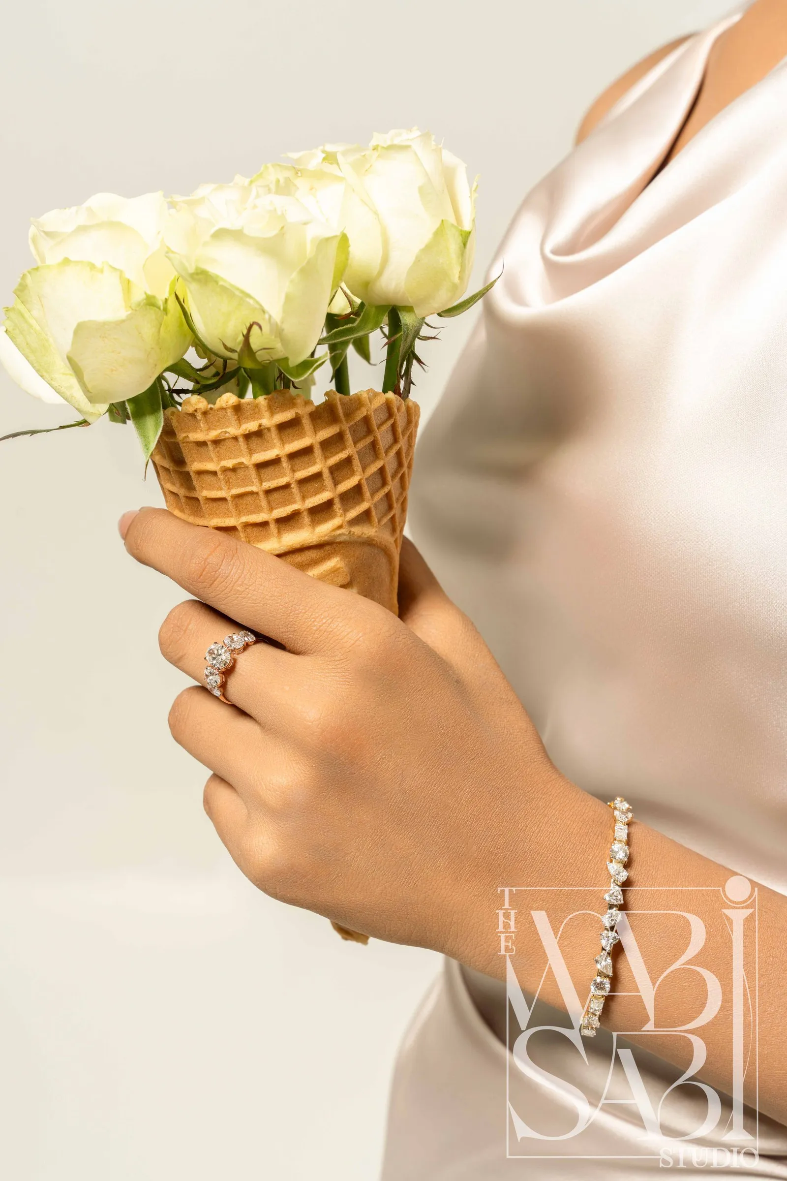 Hand holding white roses in a waffle cone, wearing a diamond ring and bracelet