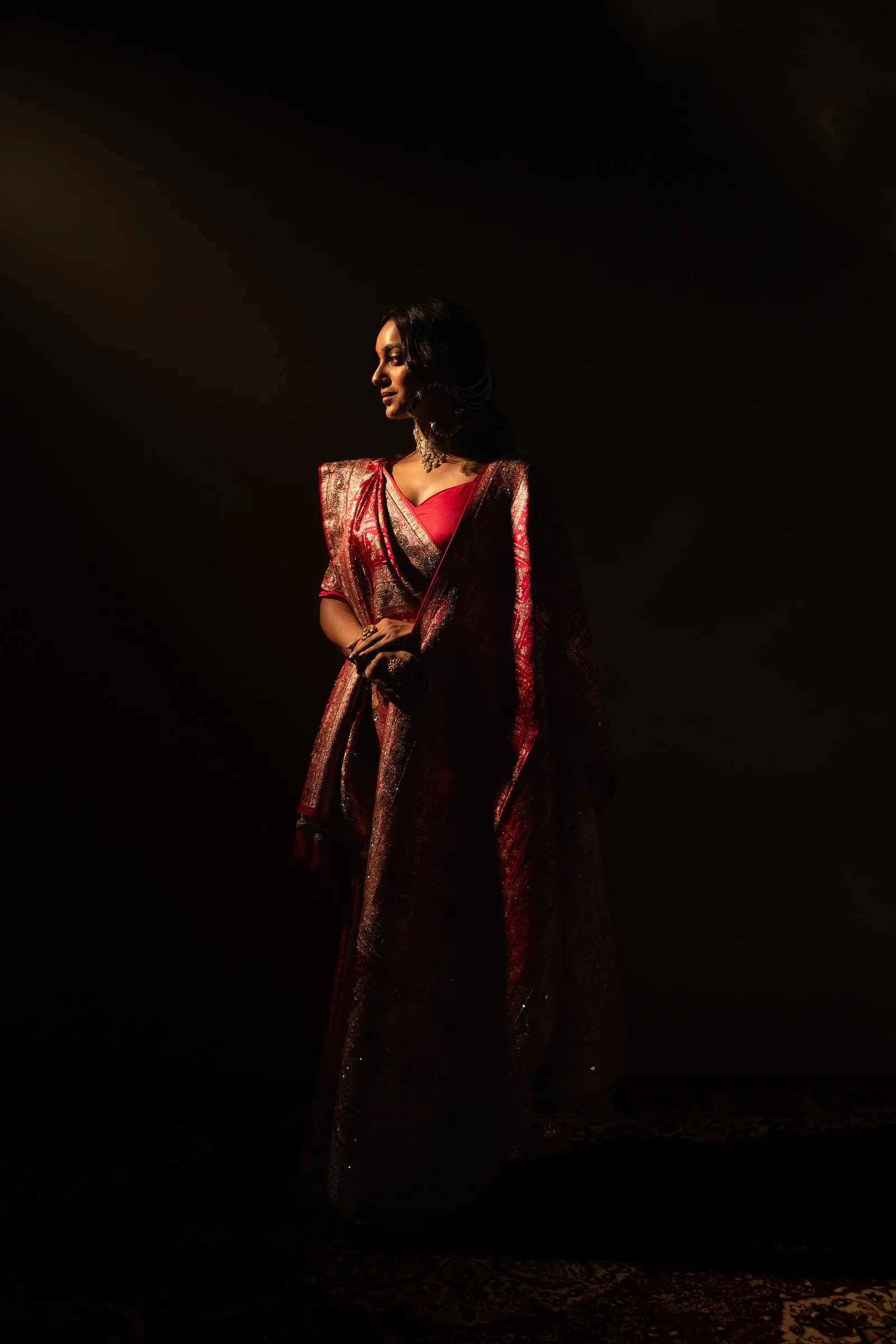 Model in a red silk saree lit by a single spotlight in the dark studio